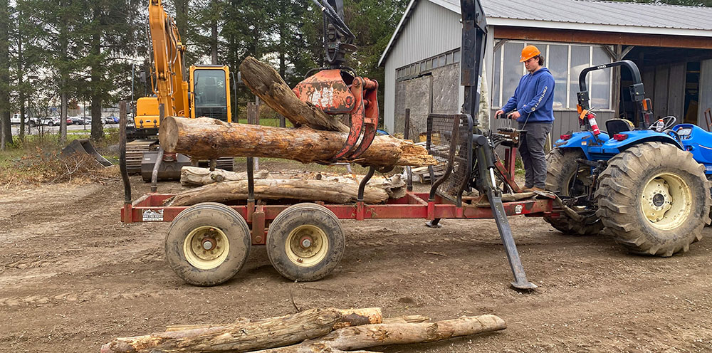 A student uses a heavy equipment to move logs.