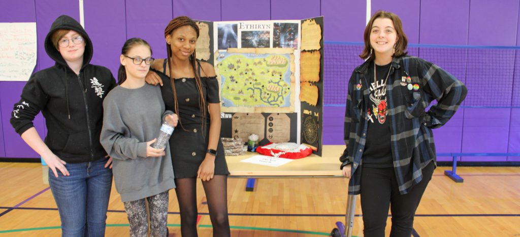 Four students standing in front of a map they created, presenting a project for the Civilizations Expo.