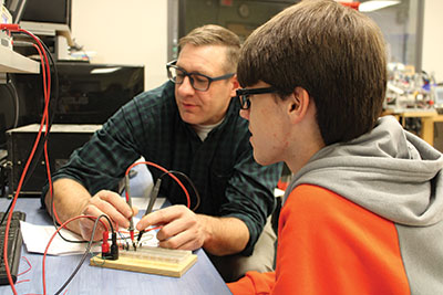 An instructor helps a student with a project at a desk.