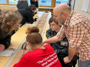 Retired Social Studies teacher David Besozzi points to the ancient Chinese scroll titled Qingming Shanghe Tu while PTECH students look on.