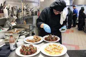 A student in the Culinary Arts program is putting garnish on a plate of sweet and sour meatballs.