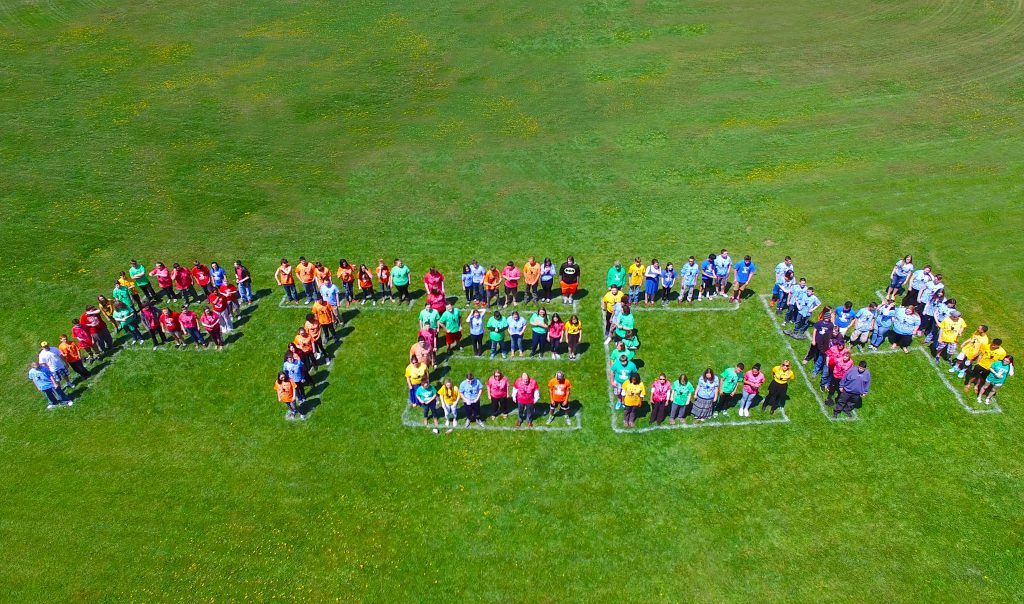 Aerial photo of PTECH students. The students are standing in a field and are aligned in a way to spell the word PTECH.