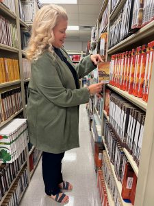 Kristi Beedon of the HFM School Library System stands in an aisle of the Instructional Resource Center while holding a book in her hand.