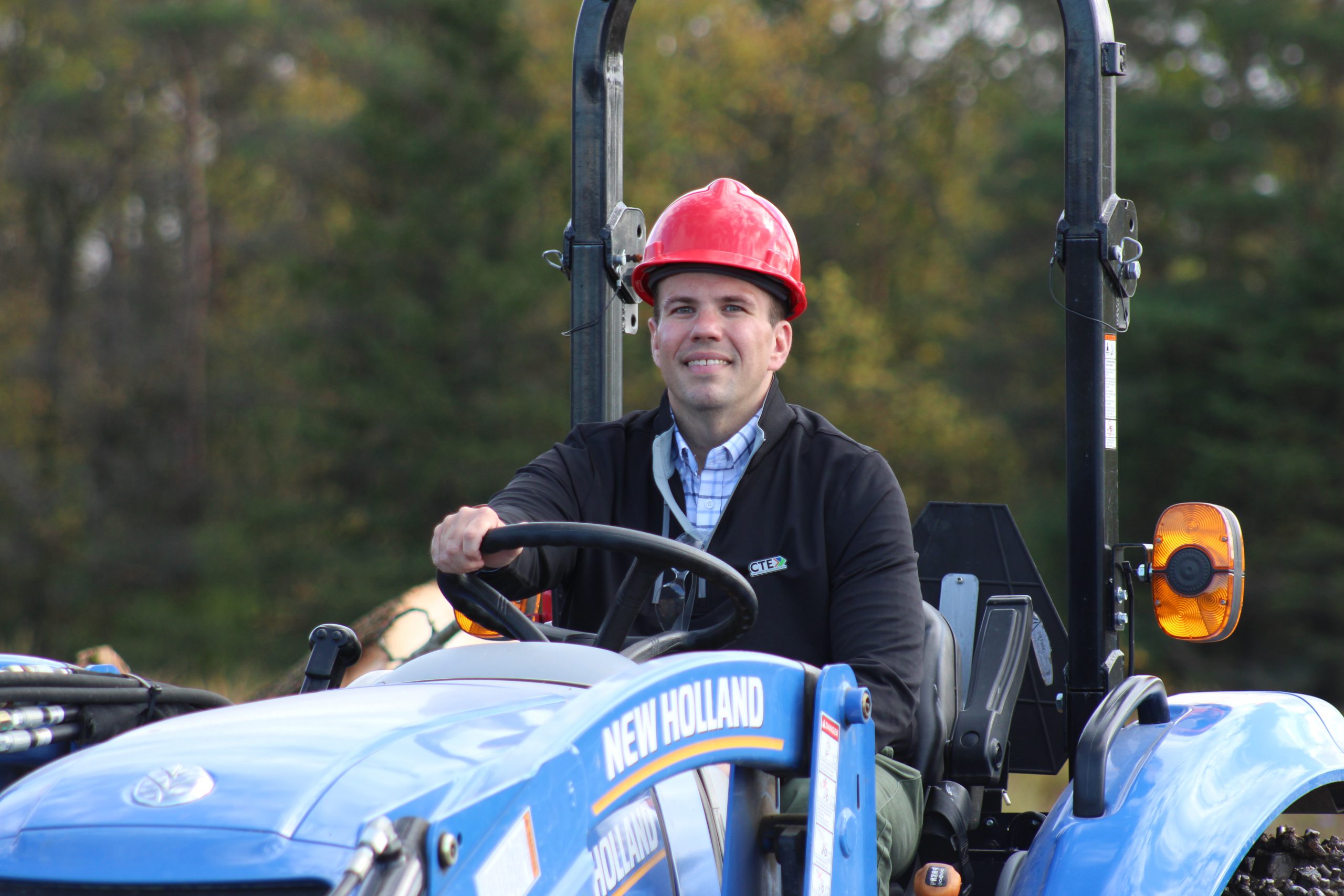 Pictured is Mike Ott, the new HFM CTE Administrative Coordinator. He is seated behind the wheel of a New Holland tractor and is wearing a hardhat while posing for the photo.