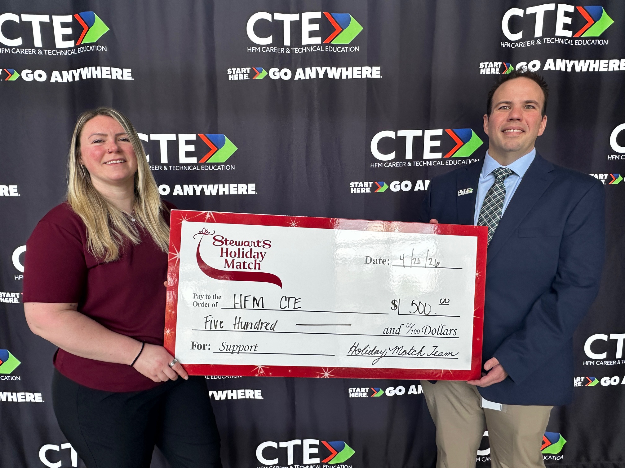 Stewart's Shops manager Brittany Capel is seen presenting an oversized celebratory check to Michael Ott. Both are standing in front of a black backdrop.